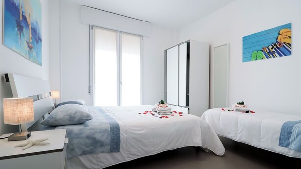 A hotel room with two beds, a desk with a lamp, and artwork on the walls.