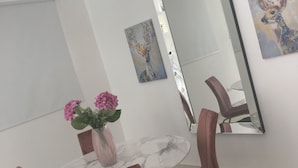 A dining area with a round table, pink chairs, a vase with flowers, and a large mirror on the wall. - IV Verdana Rental (Puñal)