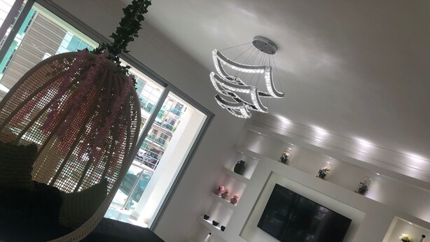 A modern living room with a large TV, white shelves, and a hanging light fixture. - IV Verdana Rental (Puñal)