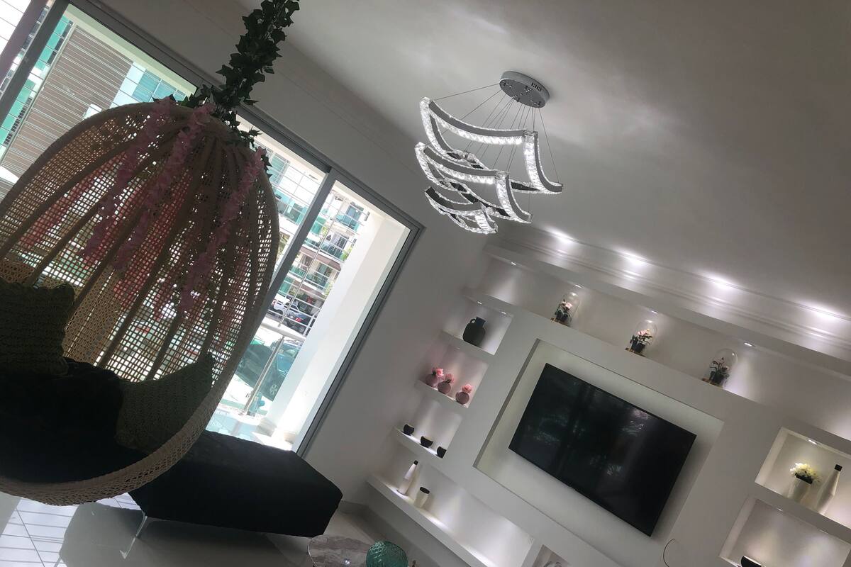 A modern living room with a large TV, white shelves, and a hanging light fixture.