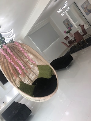 A modern interior with a hanging chair, a dining area, and a large mirror.