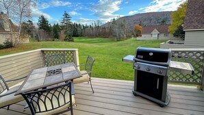 A deck with a grill, chairs, and a view of a golf course.