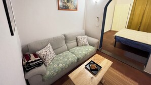 Un espacio habitable pequeño con sofá, una mesita con bandeja y una cama al fondo.