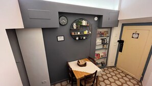Una cocina compacta con comedor, que incluye un reloj, estantes con utensilios de cocina y una puerta con un cartel.