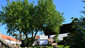 Un bâtiment avec un toit rouge et des murs blancs, entouré d’arbres verdoyants et d’un mur de pierre.