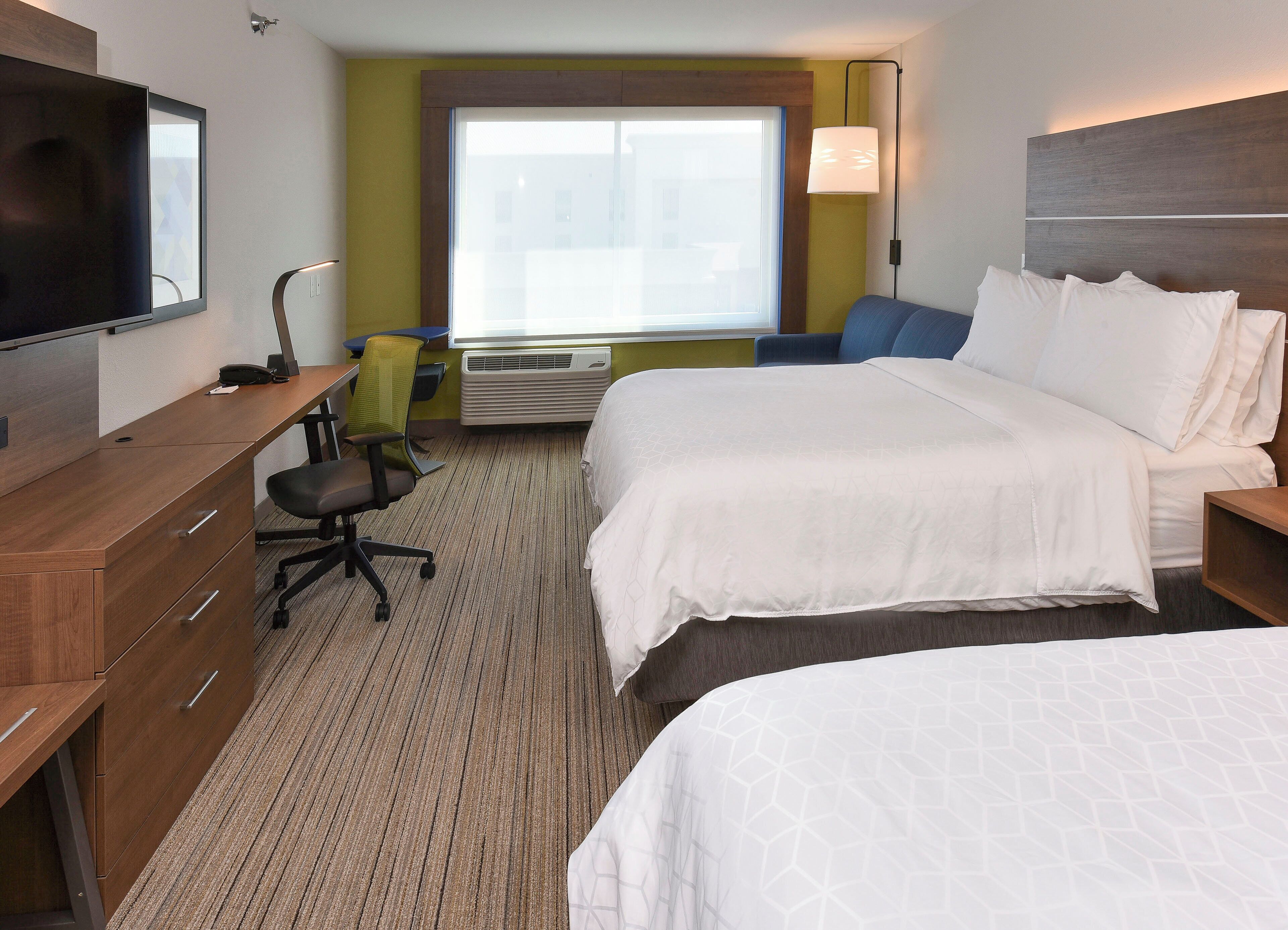 A hotel room with a bed, a desk, a chair, a television, and a window.