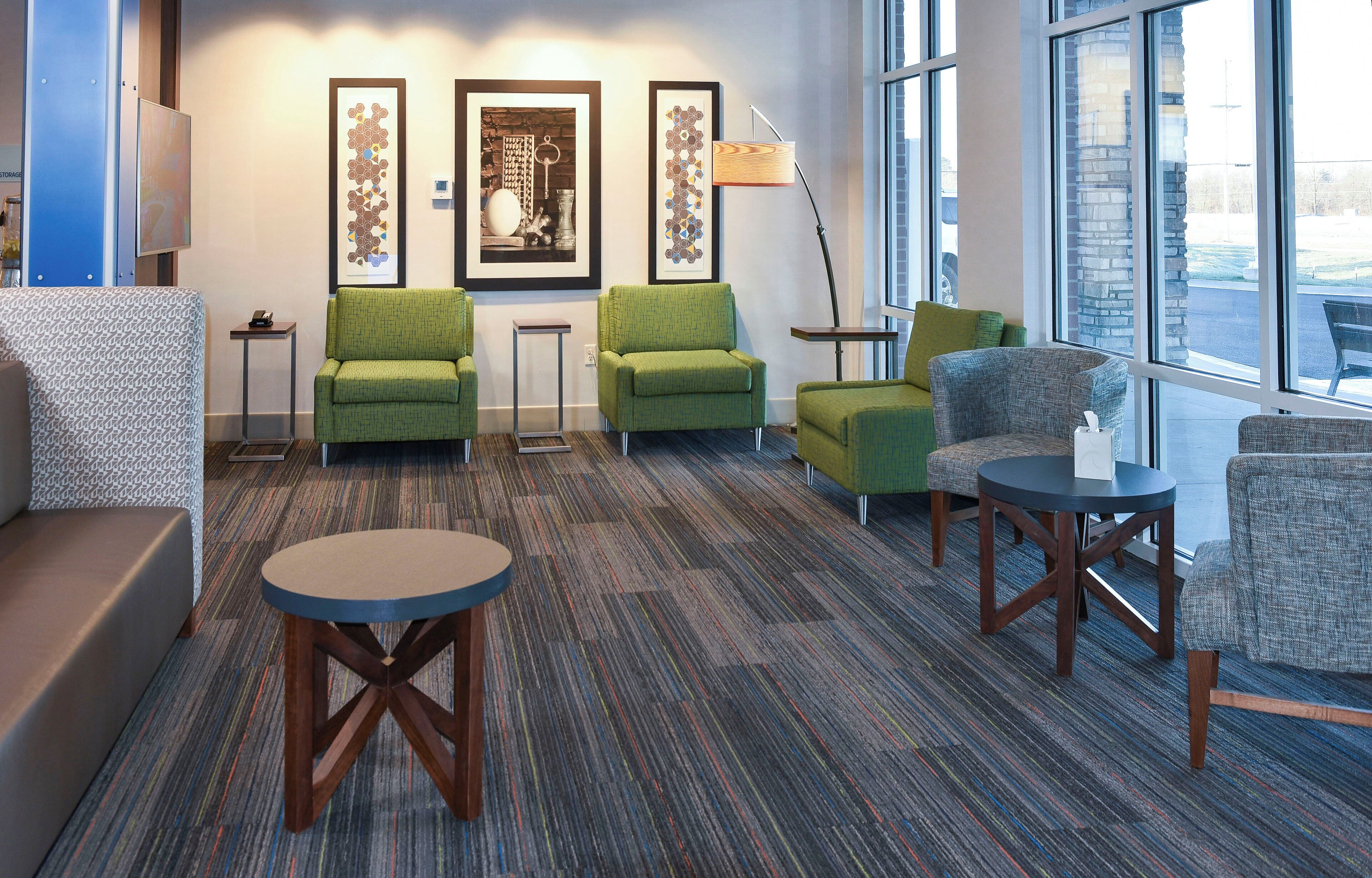 A hotel lobby with green armchairs, a round table, and a large window offering a view.