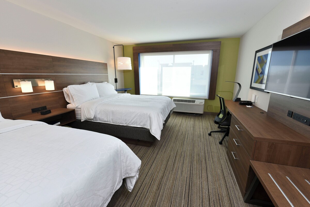 A hotel room with two beds, a desk, a TV, and a large window.
