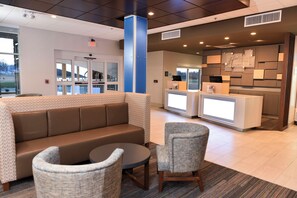 A lobby with a brown sofa, two armchairs, a small round table, and a reception desk with a computer. - Holiday Inn Express & Suites Madisonville by IHG (Madisonville)