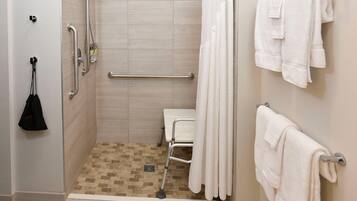 A shower with a handrail, a white towel rack, and a white towel.