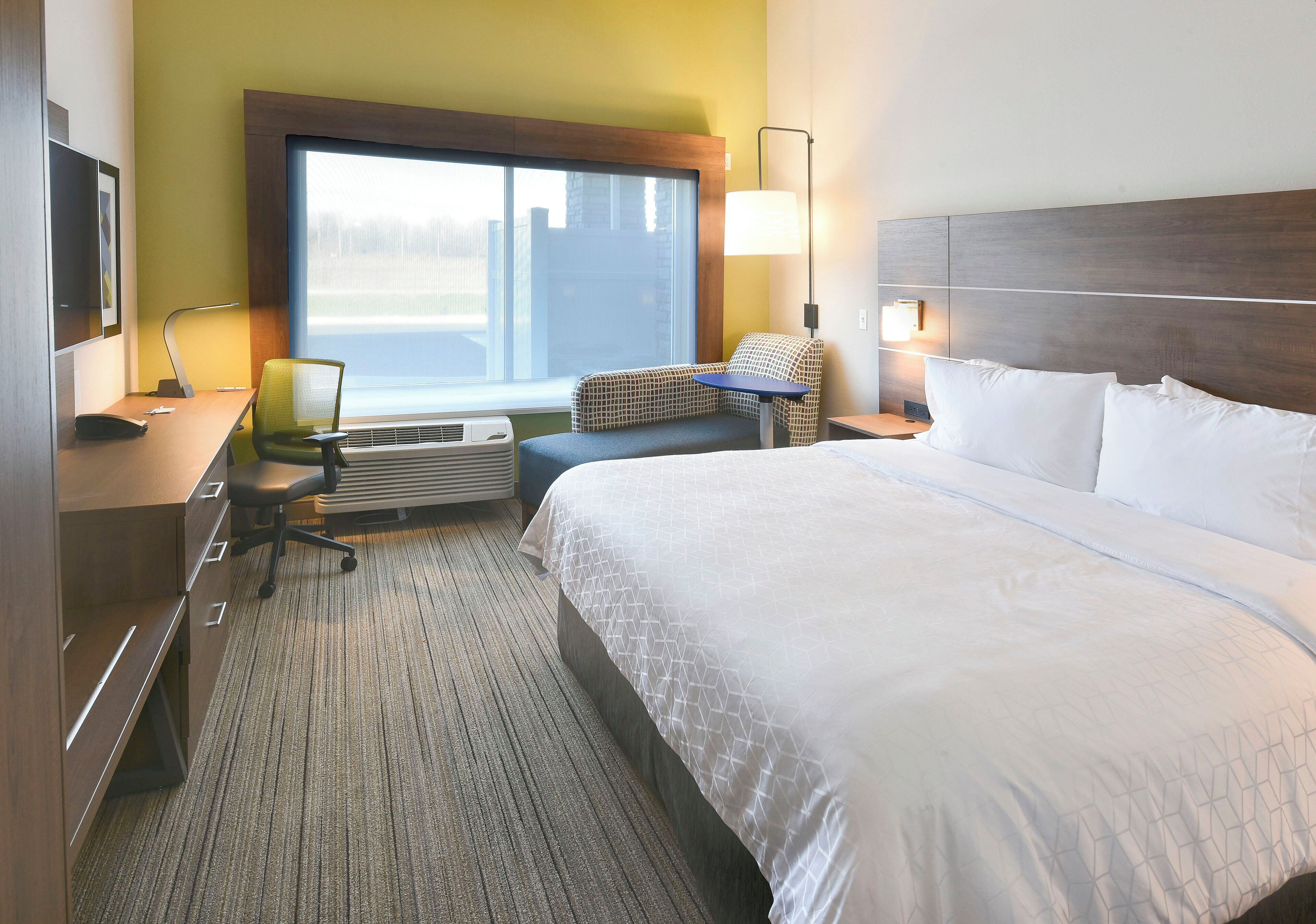 A hotel room with a large bed, a desk with a chair, a window, and a lamp.