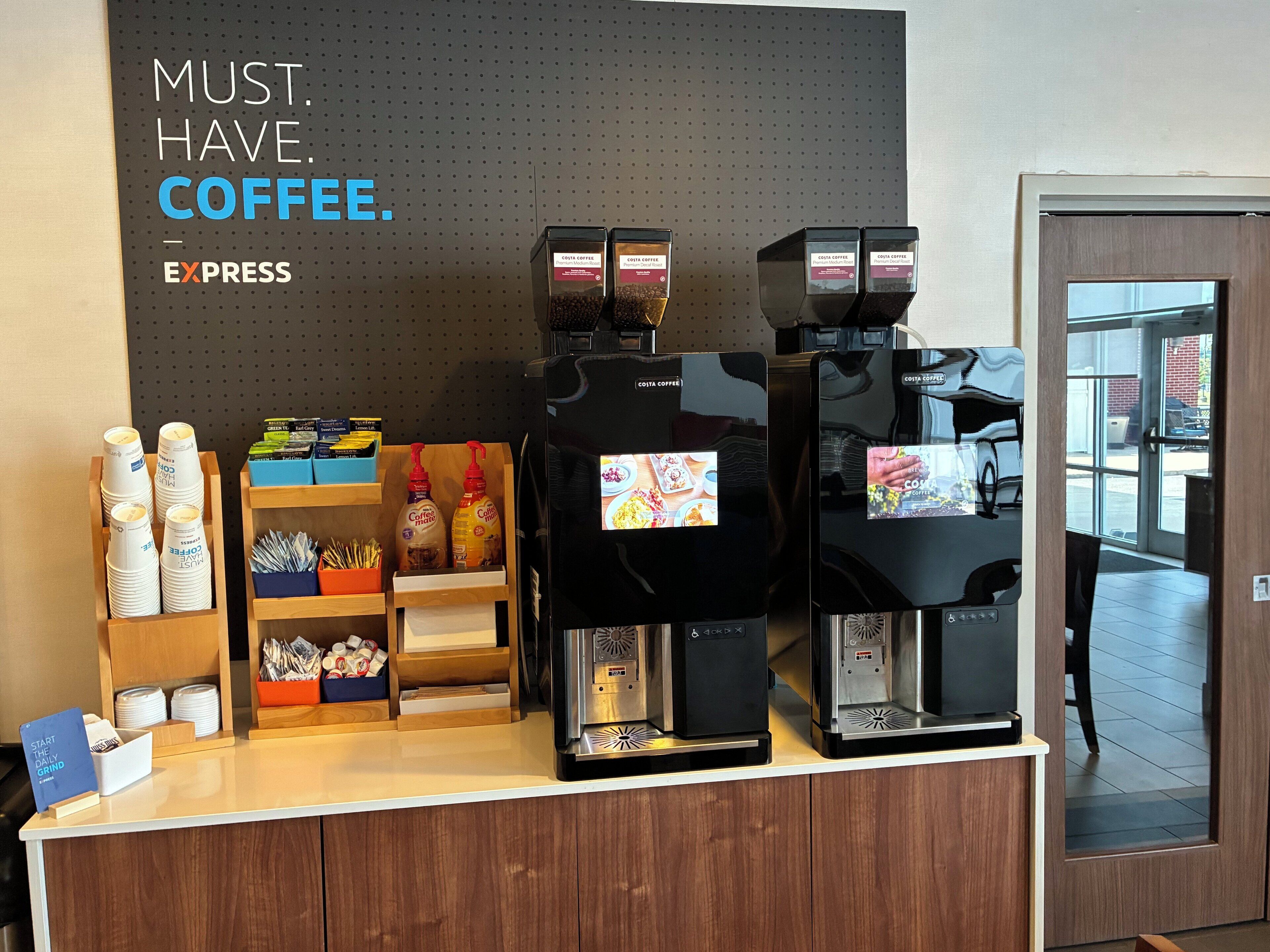 A coffee station with multiple espresso machines, disposable cups, and coffee pods.