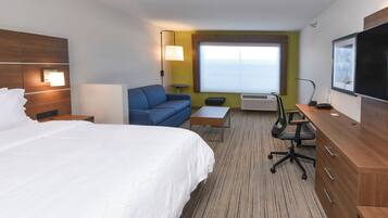 Quarto de hotel com uma cama grande, um sofá azul, uma mesa pequena, uma escrivaninha com cadeira, televisão e janela com vista.