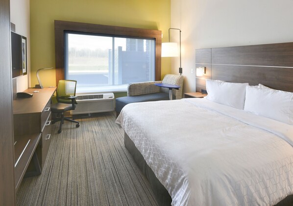A hotel room with a large bed, a desk with a chair, a window with a view, and a lamp. - Holiday Inn Express & Suites Madisonville by IHG (Madisonville)
