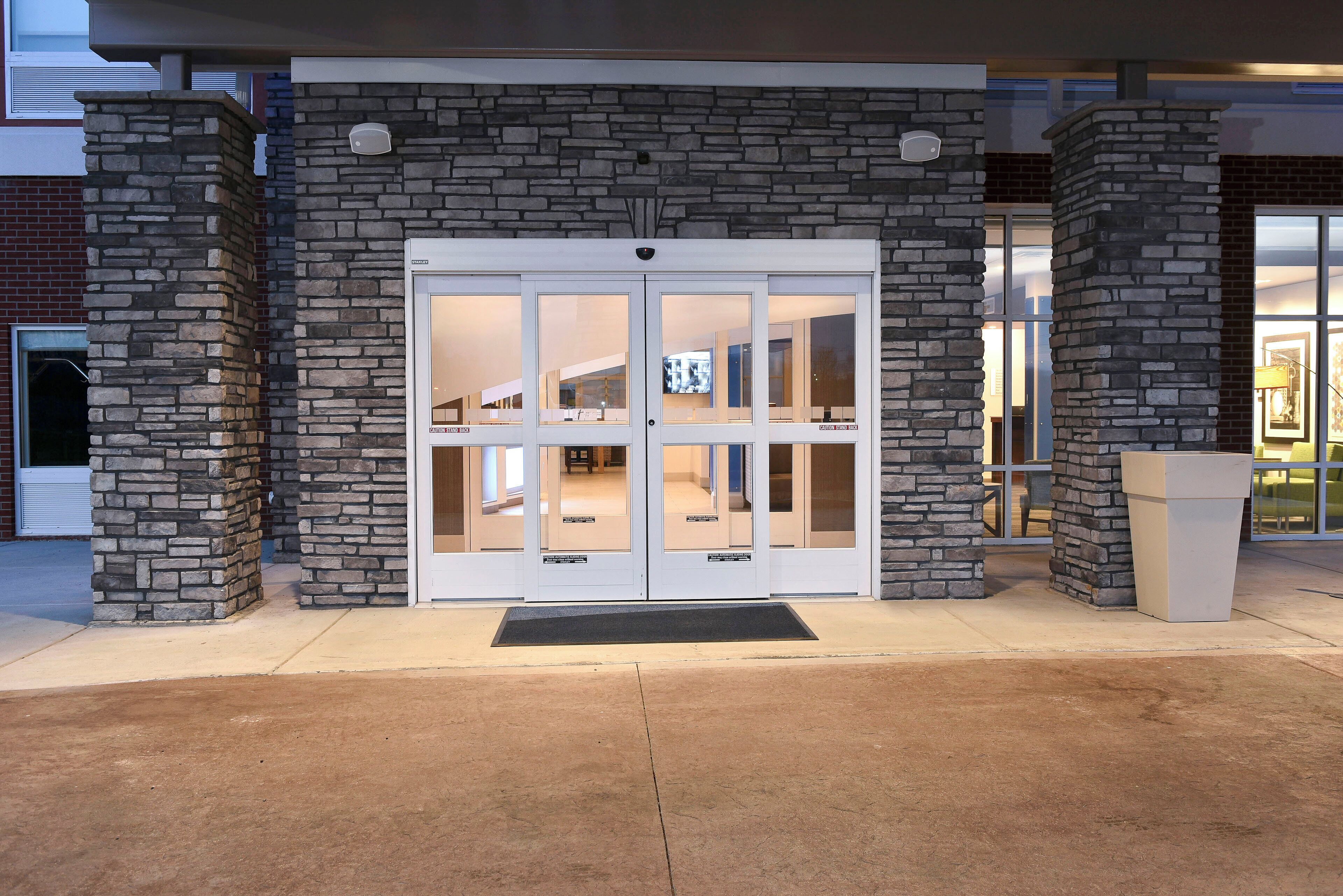 A building entrance with a stone facade, a glass door, and a doormat.