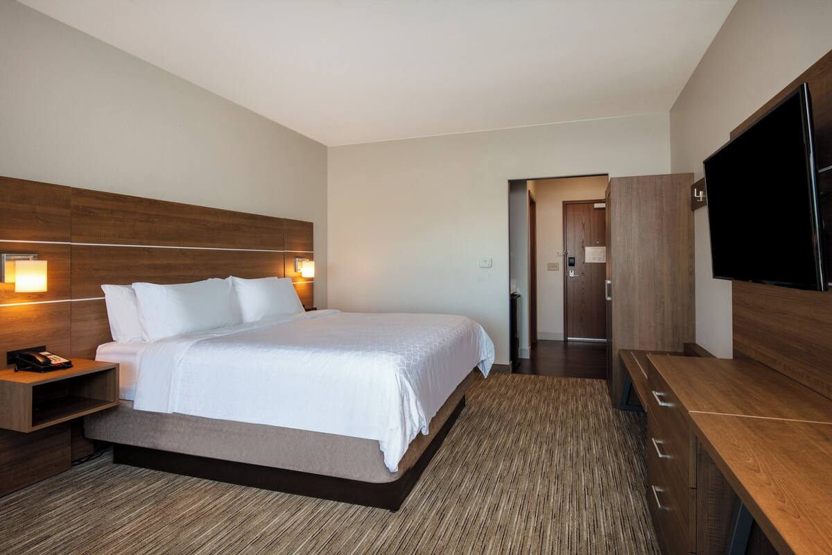 A modern hotel room with a large bed, bedside tables, a flat-screen TV, and a wooden wardrobe.