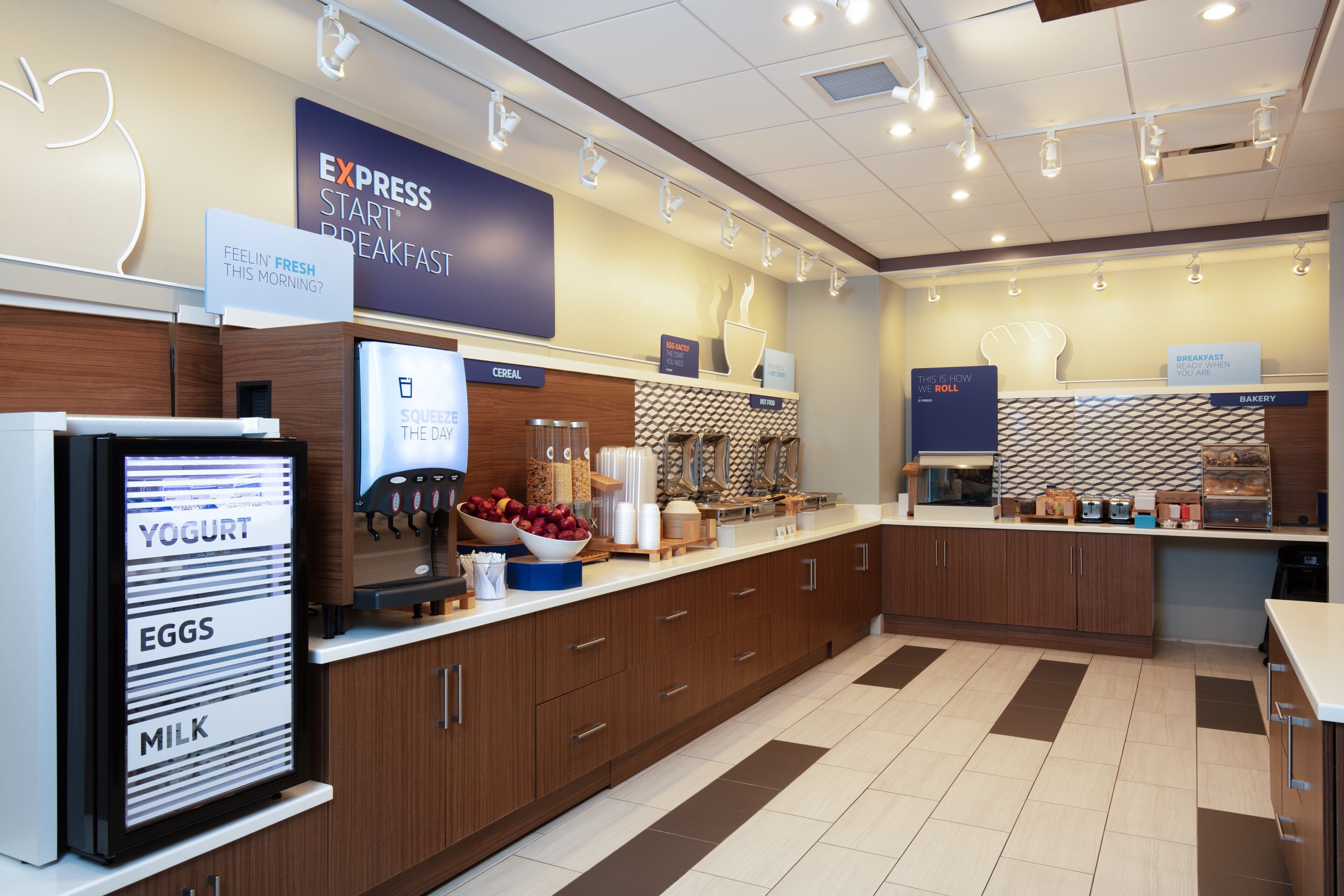 A breakfast area with labeled dispensers for yogurt, eggs, and milk, a cereal display, and a bakery section.