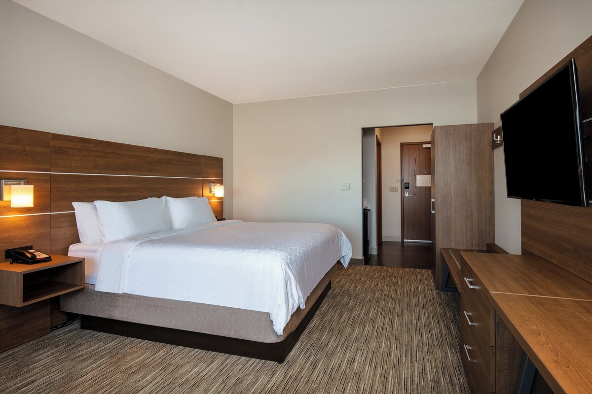A modern hotel room with a large bed, bedside tables, a flat-screen TV, and a wooden wardrobe.