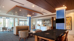 A modern hotel lobby with a reception desk, seating area, and a large black table. - Holiday Inn Express & Suites Beloit by IHG (Beloit)