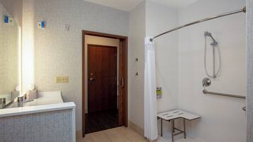A bathroom with a shower, a sink, a mirror, and a door leading to another room.
