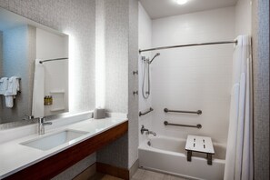 A modern bathroom with a large mirror, two sinks, a shower with grab bars, and a small stool. - Holiday Inn Express & Suites Beloit by IHG (Beloit)