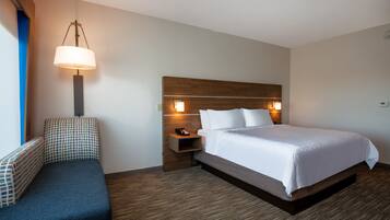 A hotel room with a bed, bedside table, lamp, and a bench.