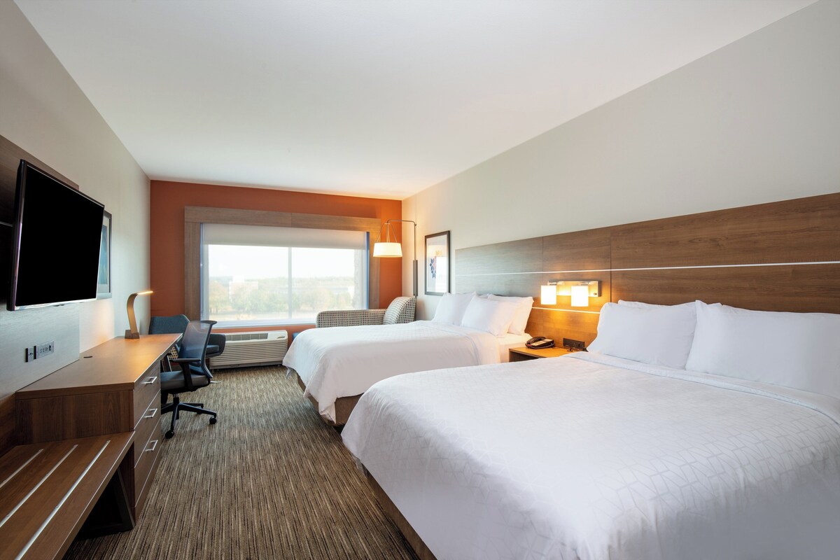 A hotel room with two beds, a desk, a chair, a TV, and a window with a view.