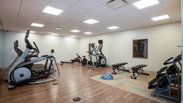 Una palestra con macchinari cardio, pesi liberi e uno specchio.