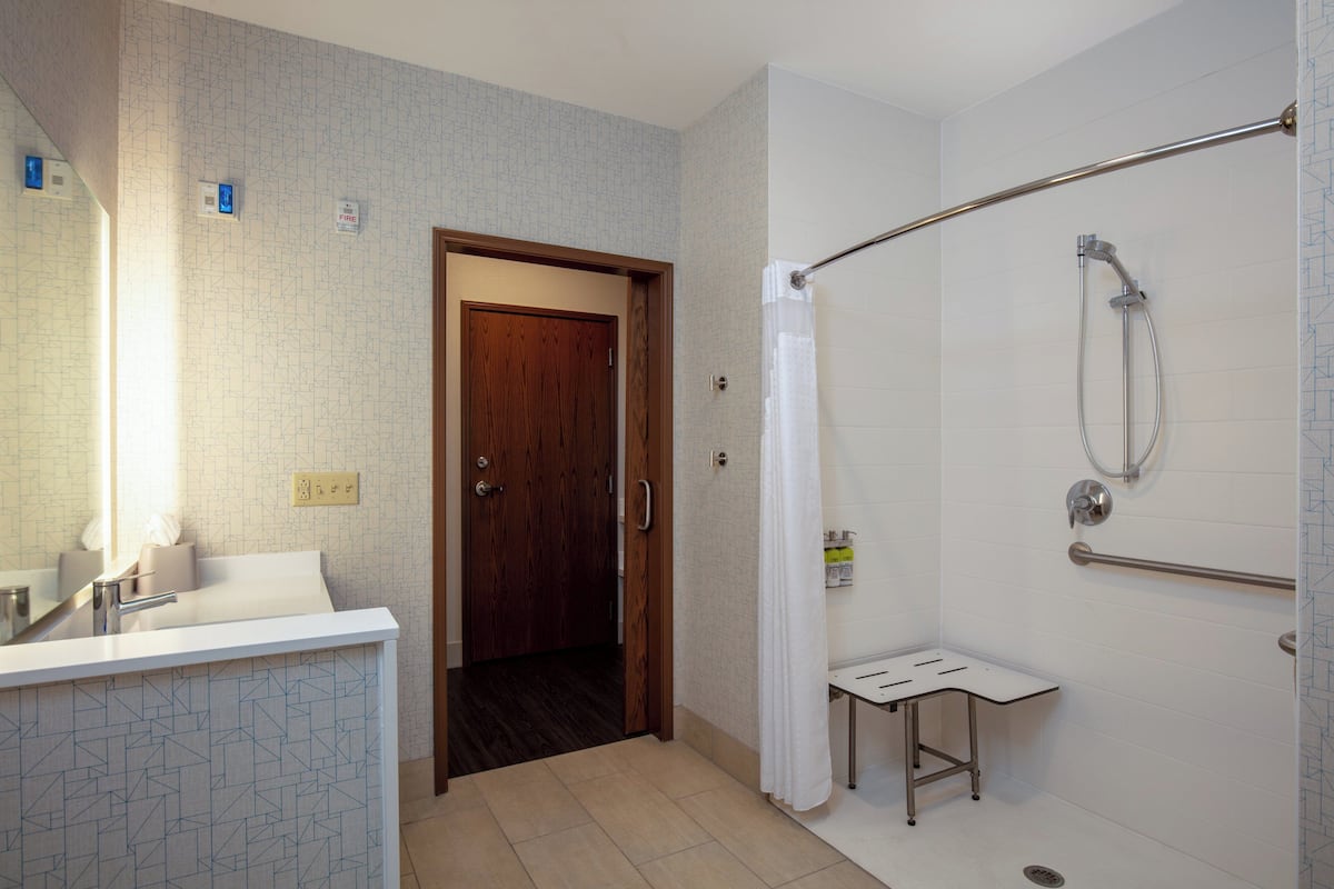 A bathroom with a shower, a sink, a mirror, and a door leading to another room.