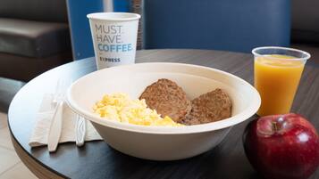 A breakfast tray with scrambled eggs, sausage patties, a red apple, a cup of coffee, and a glass of orange juice on a round table.