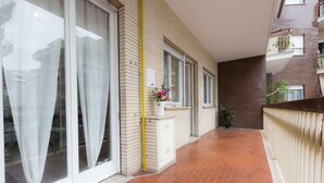 Un pasillo con suelo de baldosas, una puerta blanca y una ventana con cortinas translúcidas.