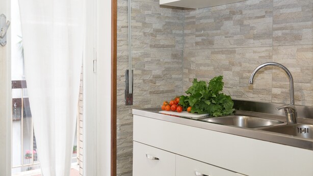 Una cocina moderna con protector de piedra, pileta de acero inoxidable y una ventana con cortinas.