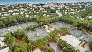 An aerial view of a residential area with multiple tennis courts surrounded by dense greenery and a coastline in the background. - WaterColor Condo‑Retreat | 2.5BR/2BA - Bikes, Balcony, Walk to Beach Club (Santa Rosa Beach)