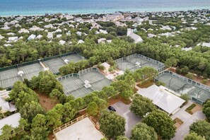An aerial view of a residential area with multiple tennis courts surrounded by dense greenery and a coastline in the background. - WaterColor Condo‑Retreat | 2.5BR/2BA - Bikes, Balcony, Walk to Beach Club (Santa Rosa Beach)