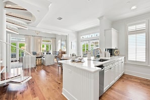 A spacious kitchen with a central island, white cabinetry, and a view of the outdoors through large windows.