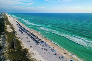 A beach with rows of umbrellas and sun loungers, a walkway, and the ocean.