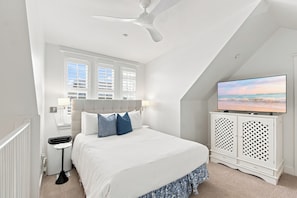A bedroom with a bed, a ceiling fan, a TV, and a window with blinds.
