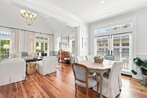 A spacious living room with a dining area, wooden flooring, and large windows with shutters.