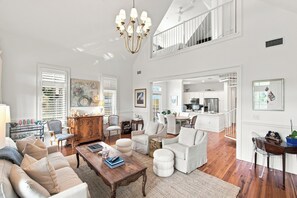 A spacious living room with a high ceiling, a dining area, and a kitchen with white cabinetry.