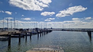 A marina with boats docked, a pier extending into the water, and a clear sky with clouds.