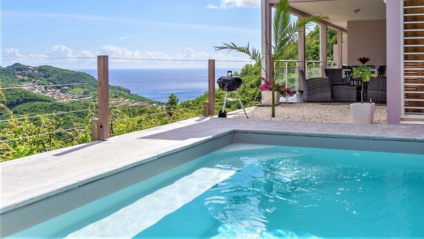 Une piscine avec vue sur l’océan et les collines, un barbecue et un espace salon extérieur.