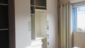 Een slaapkamer met een witte garderobe, een bed en een raam met gordijnen.