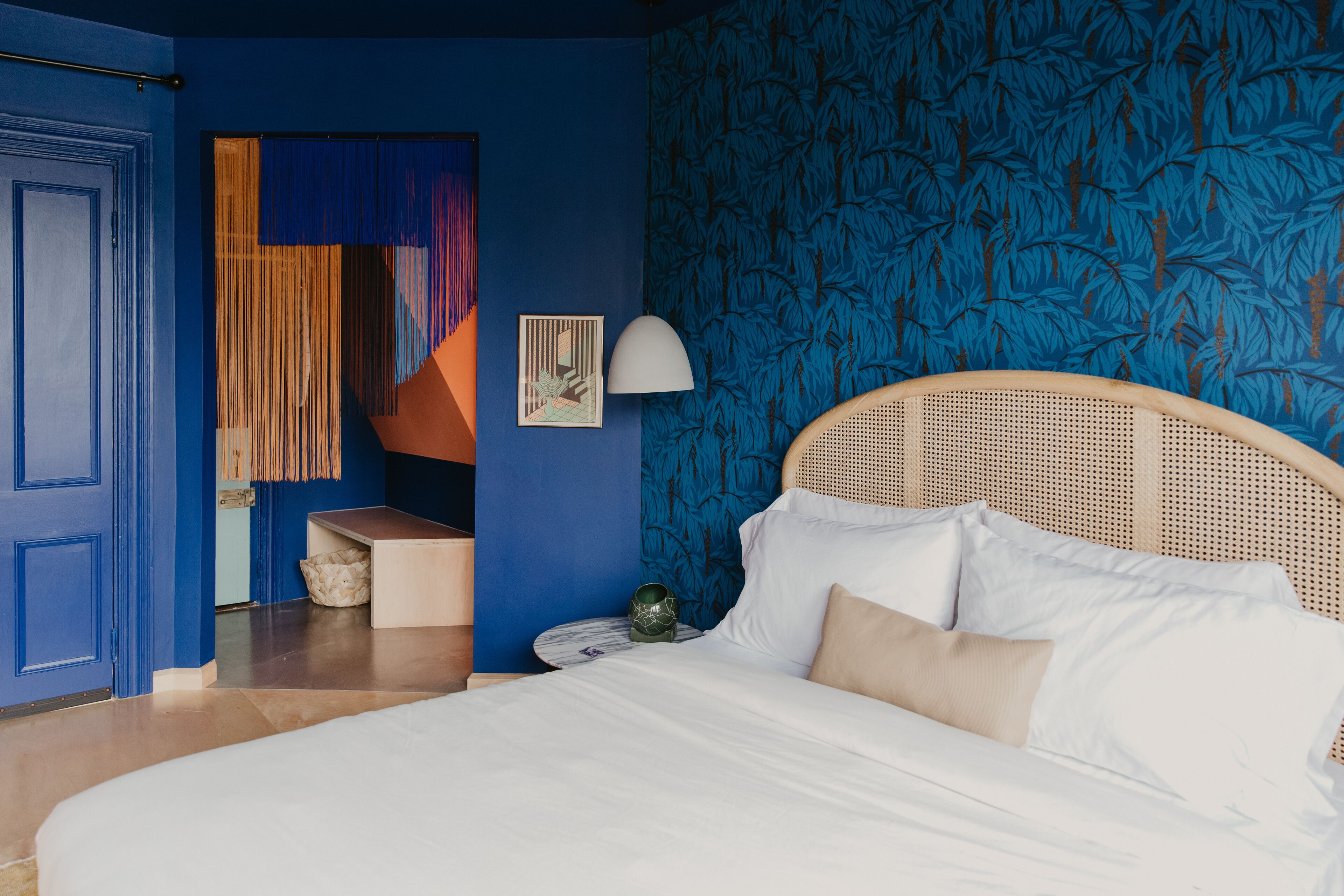 A bedroom with a bed, a nightstand, a lamp, and a blue patterned wall.