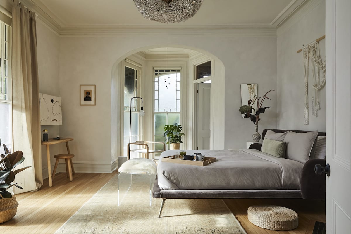 A bedroom with a bed, bedside table, chair, and a view of a balcony.