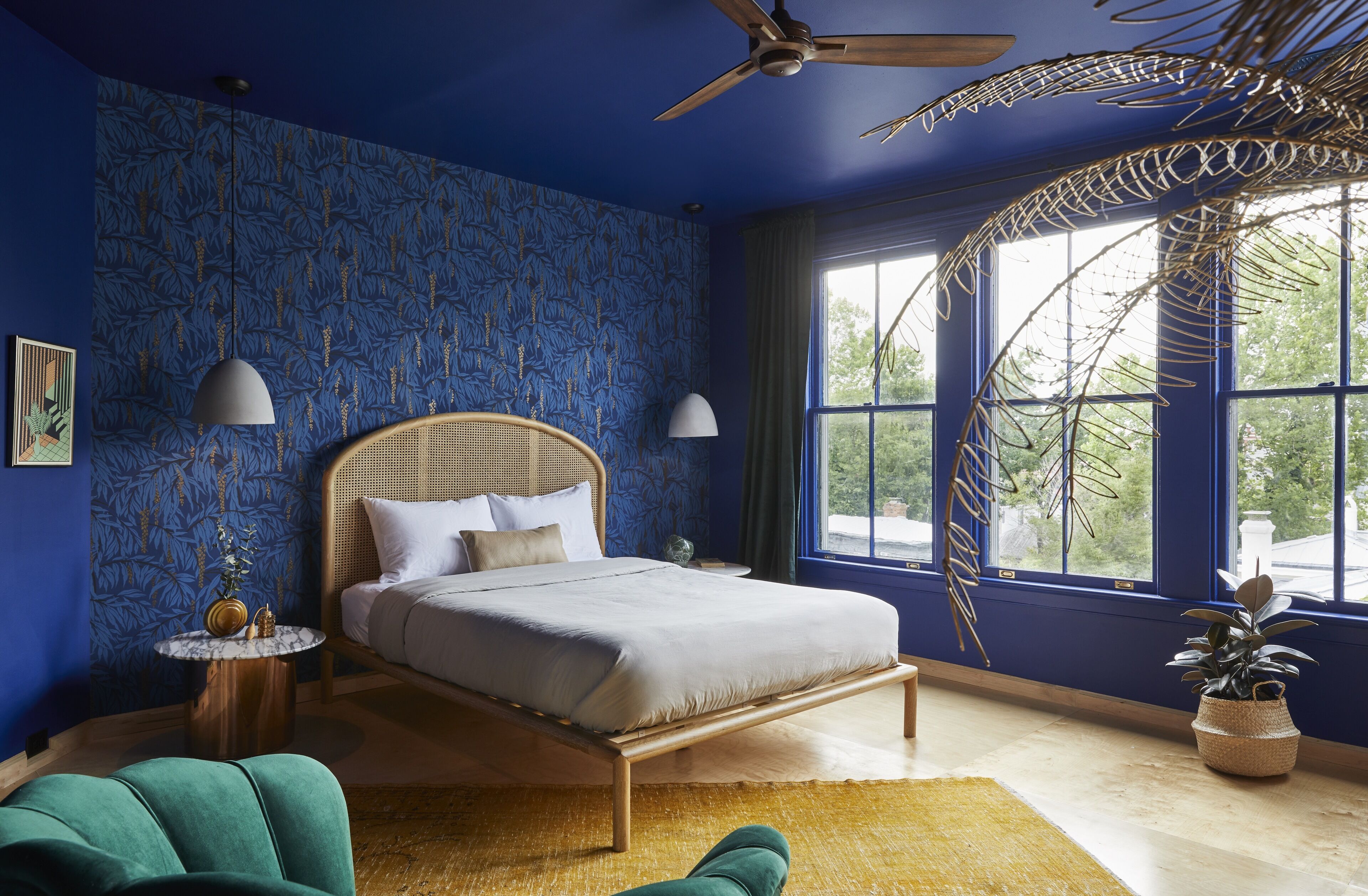 A bedroom with a bed, a ceiling fan, a window with a view, and a decorative plant.