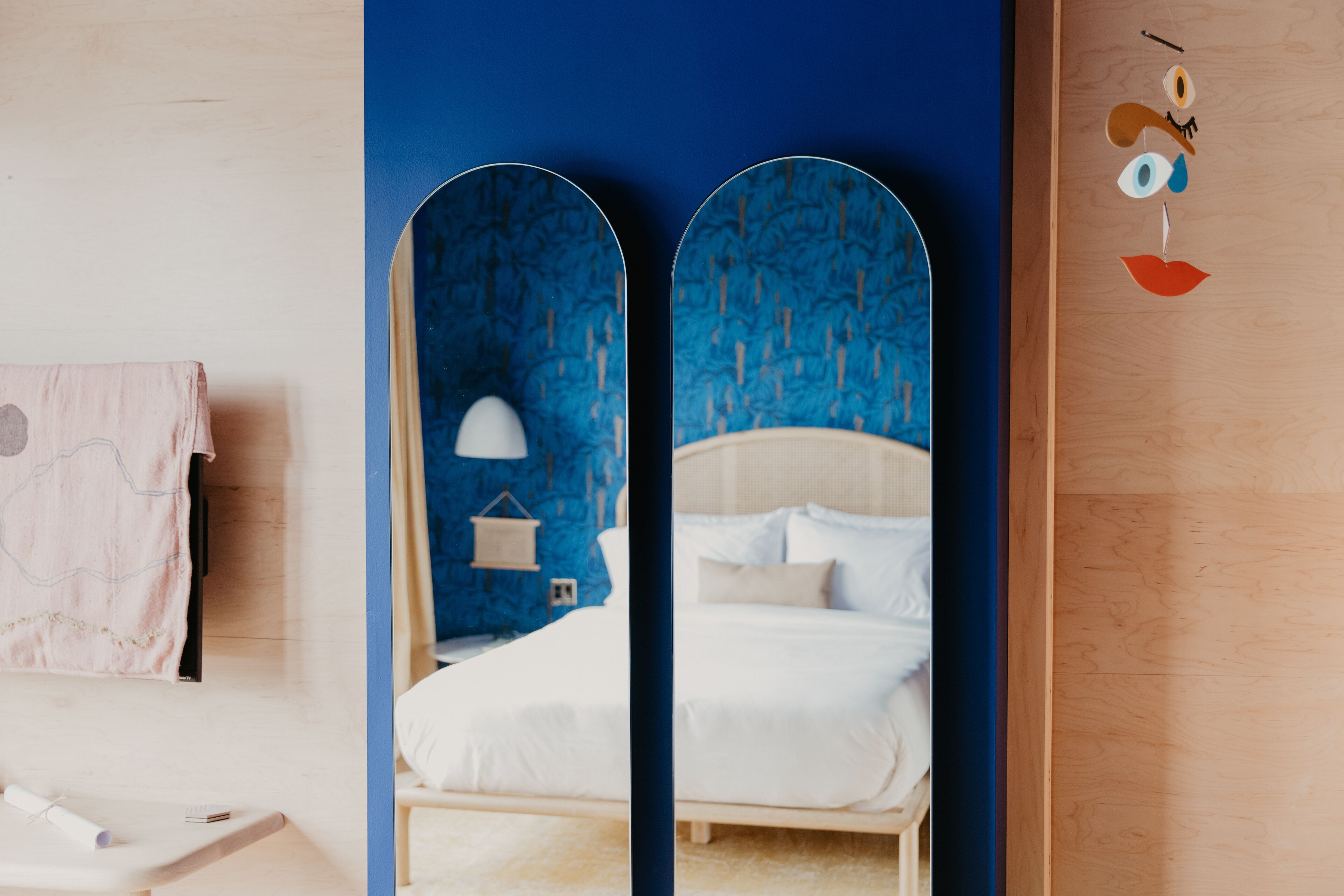 A bedroom with a bed, a nightstand, a lamp, and a wall-mounted mirror.