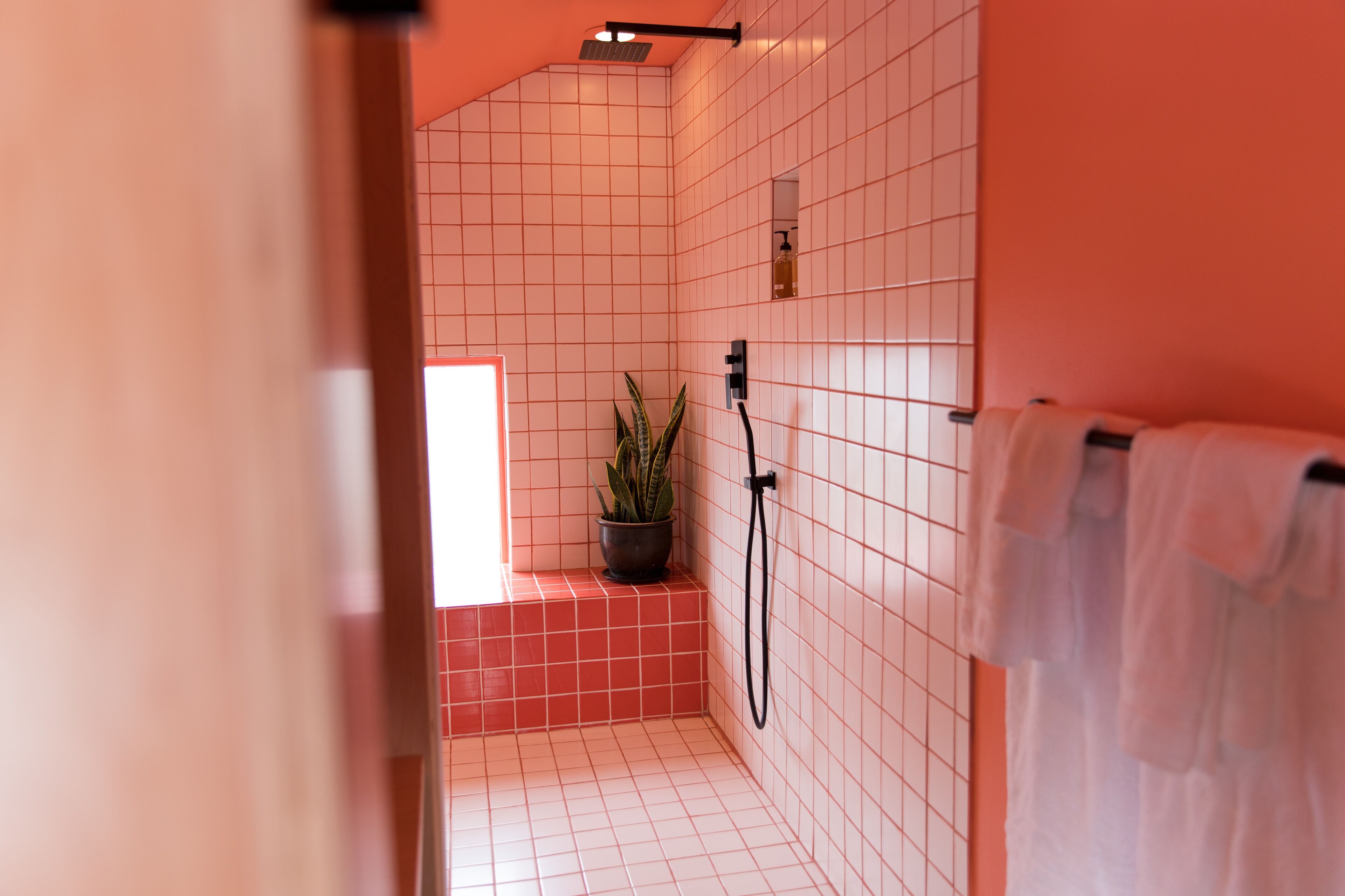 A bathroom with white tiled walls and floor, a potted plant, a shower, and a towel rack.