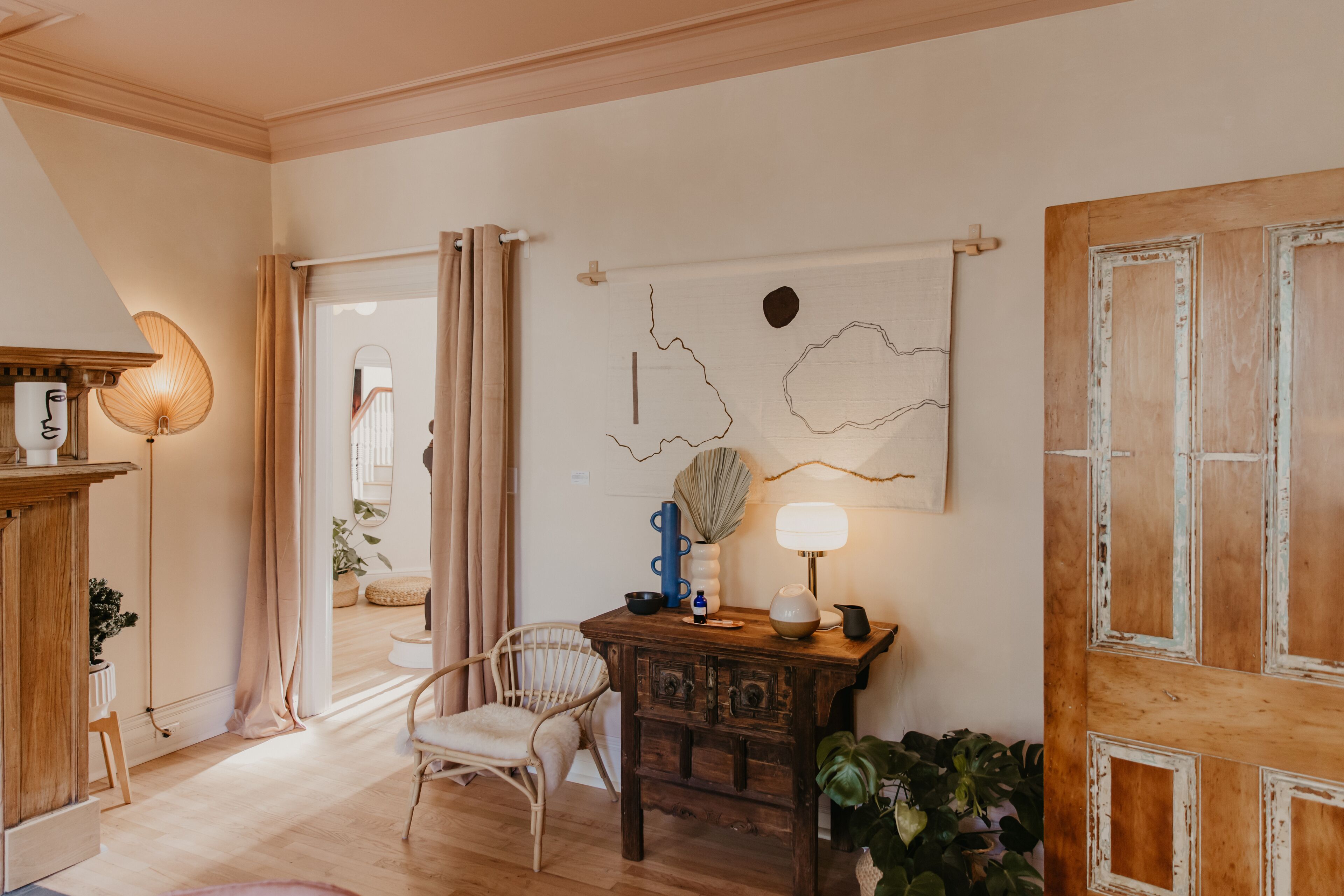 A room with a wooden floor, a wooden table with a lamp, a chair, and a door with a rustic design.