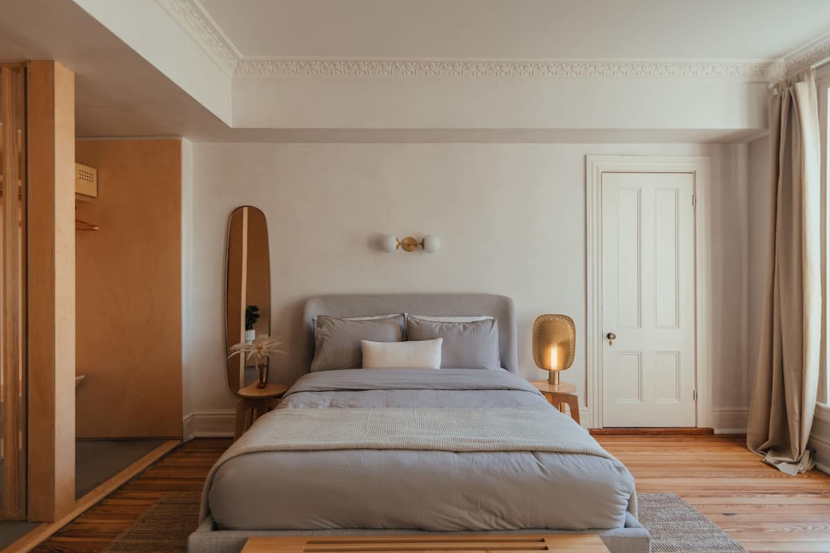 A bedroom with a bed, a nightstand, a mirror, and a door.