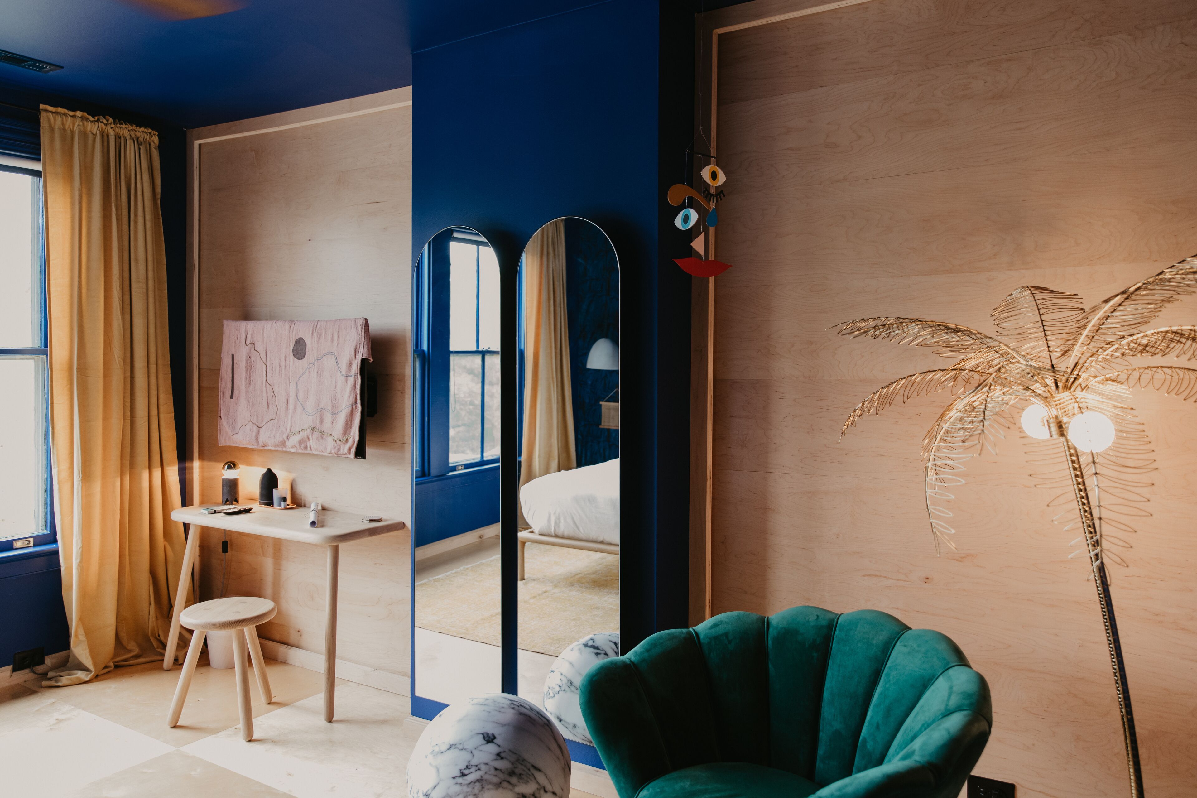 Una stanza con una scrivania in legno, una sedia verde, un grande specchio e una lampada da terra decorativa.